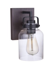 The Foxwood - 53601-FBDT wall-mounted sconce blends industrial design with vintage and modern elements. It features a black metal bracket, clear glass shade, exposed Edison-style bulb, and a wooden finish backplate that contrasts elegantly with its sleek