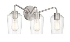 The Shayna - 56103 is a modern wall-mounted light fixture with a brushed metal finish, featuring three clear glass shades housing exposed filament bulbs and elegantly extending arms from a circular base.