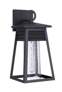 The Becca - ZA2714-TB is a black outdoor wall lantern with a coastal vibe, featuring a geometric design and louvered detail. It has clear cylindrical glass housing with a vintage filament bulb, all in Textured Matte Black finish, complemented by a square