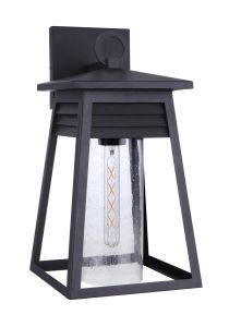 The Becca - ZA2724-TB is a modern outdoor wall lantern featuring a black metal frame and clear cylindrical glass. It houses an Edison-style bulb, with a tapered design and small square backplate, offering a coastal aesthetic that complements louvered deta