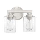 The Bolden - 50502 dual sconce light fixture showcases a brushed metal base with two clear seeded glass shades, each encasing an exposed Edison bulb. Mounted on a circular backplate, it adds elegant charm to any space.